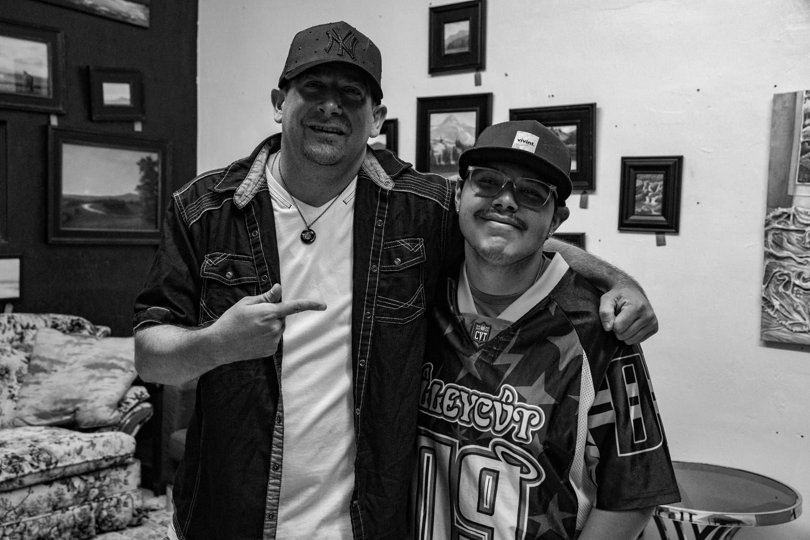 Black and white shot of Dill the Menace posing with a friend in front of the gallery's framed artwork
